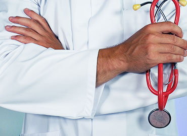 Doctor in a white coat with arms crossed over his chest, holding red stethoscope.