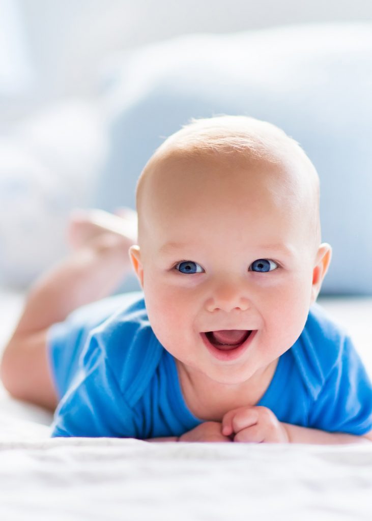 Baby boy in white sunny bedroom laying on his belly and smiling.