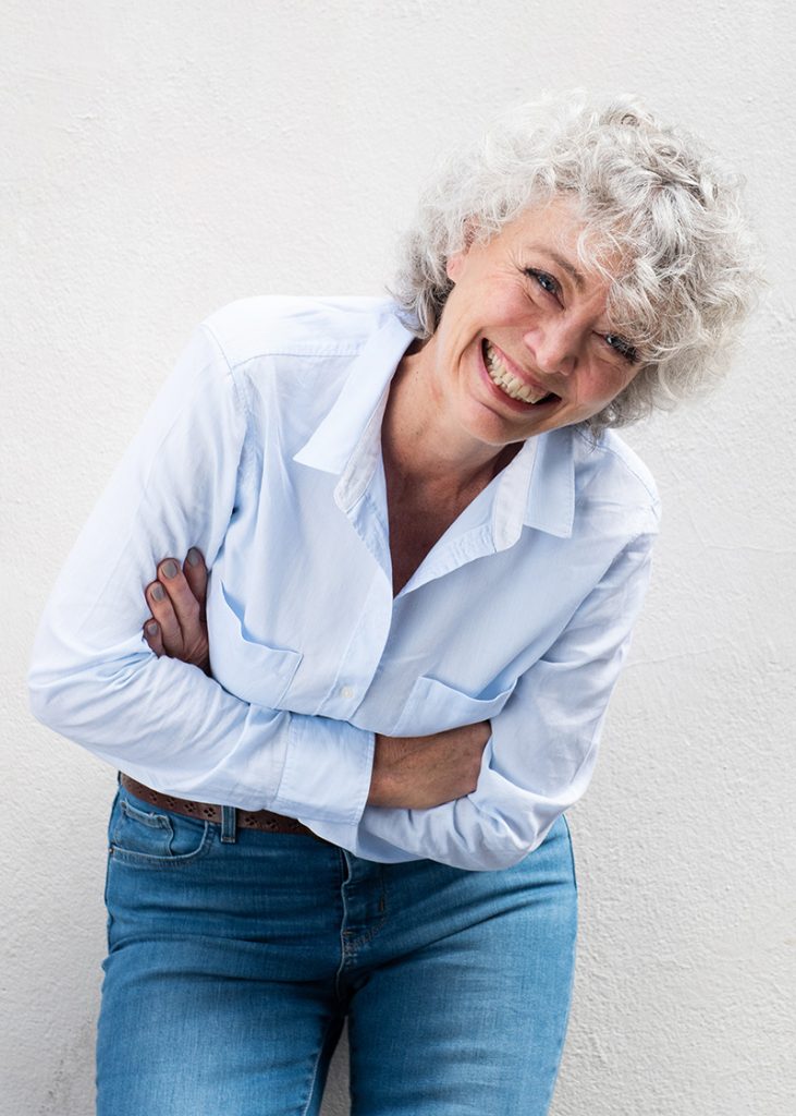 Portrait of older woman laughing with arms crossed by gray wall