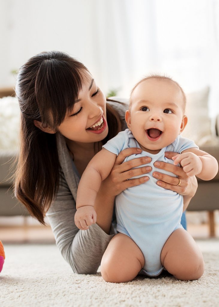 Smiling young asian mother with little baby at on the floor.