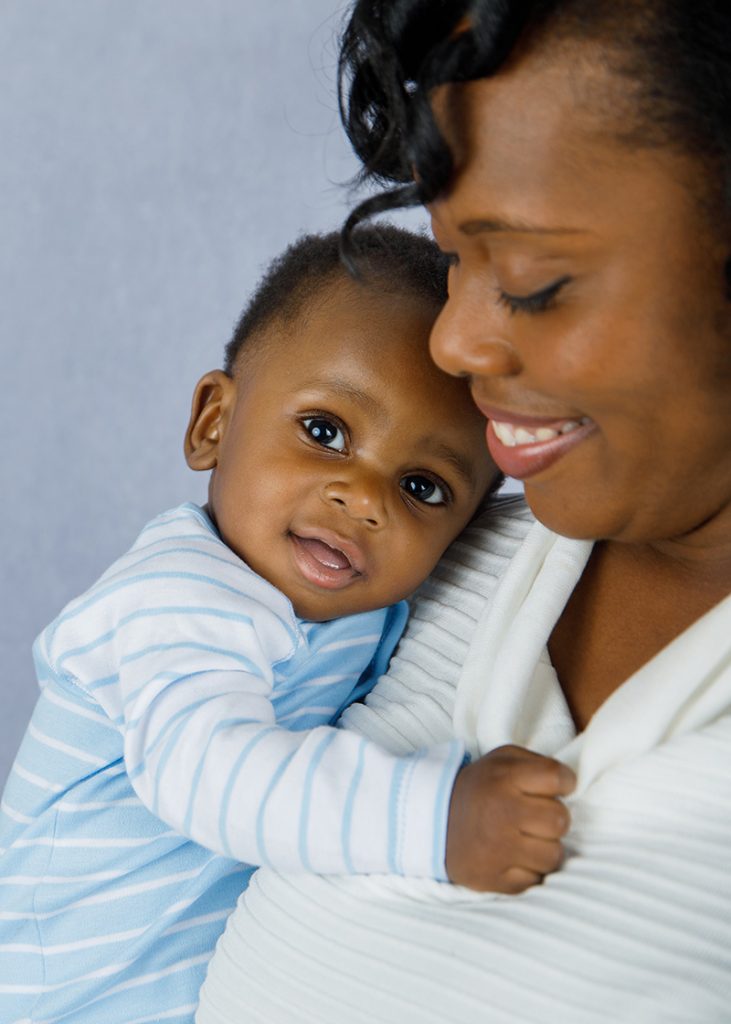 Black woman holding her baby and smiling with blue background