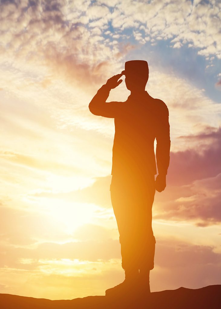 Soldier saluting with the sunset behind him