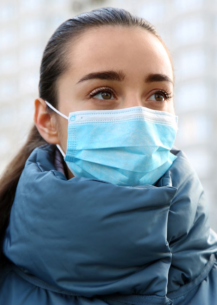 Brown haired white woman wearing winter jacket and blue disposable face mask.